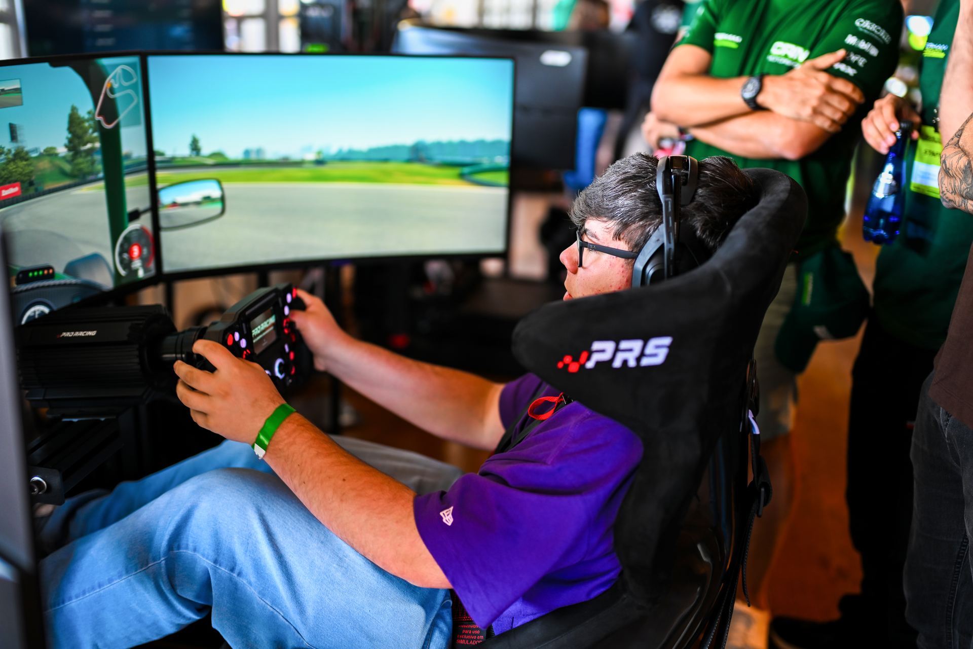 Piloto concentrado no simulador, mãos no volante, diante das telas com a pista